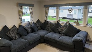 A sectional sofa with patterned cushions, a window with curtains, and a view of mobile homes outside. - Come to the finest coast line in Britain! (Prestonpans)