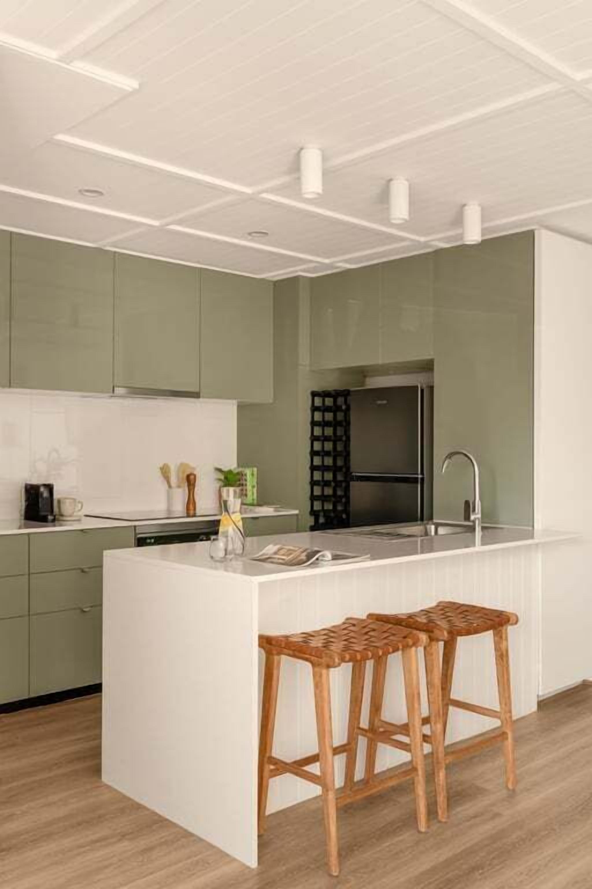 A modern kitchen with green cabinets, a white countertop, and a built-in island with bar stools.