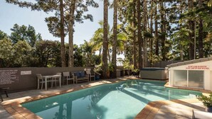 Uma piscina cercada por árvores altas, com área de estar e aviso contra a escalada no telhado.