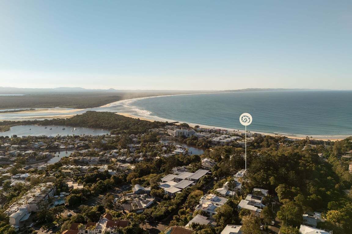 An aerial view of a coastal town with a beach, clear skies, and a prominent sign indicating a location.