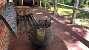 A covered outdoor seating area with a metal chair and a wicker table lamp.