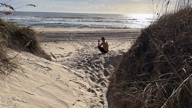 A sandy beach with a person sitting and looking at the ocean.