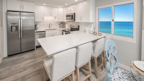 Een moderne keuken met witte kasten, roestvrijstalen apparatuur en een groot eiland met barkrukken.