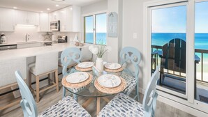Een moderne keuken met witte kastjes, een centraal eiland en een eethoek met een glazen tafel en blauwe stoelen.