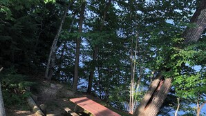 Eine Holzterrasse mit Picknicktisch und Bänken, umgeben von Bäumen und einem Gewässer.