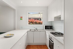 Uma cozinha moderna com armários brancos, micro-ondas embutido, fogão a gás e janela com vista para folhagem de outono.