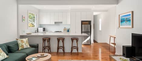 Un espacio habitable moderno con cocina, comedor y zona de estar con sofá y taburetes de bar.