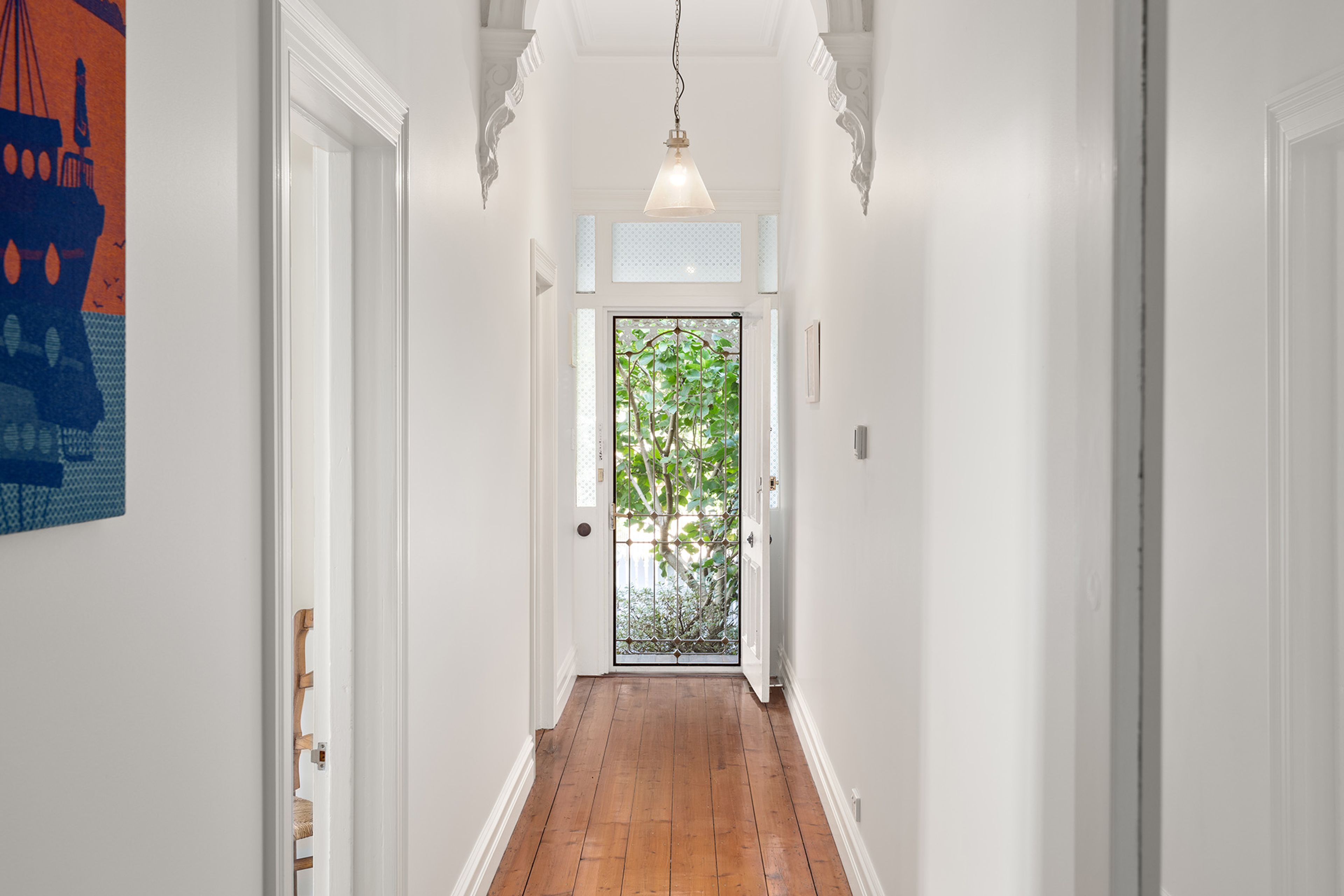 A hallway with white walls, a wooden floor, and a door with a metal gate.