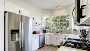 Uma cozinha moderna com armários brancos, eletrodomésticos de aço inoxidável e uma janela grande que traz luz natural.