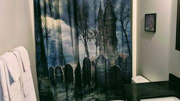 A bathroom with a gothic-themed shower curtain, a white toilet, and a black countertop.