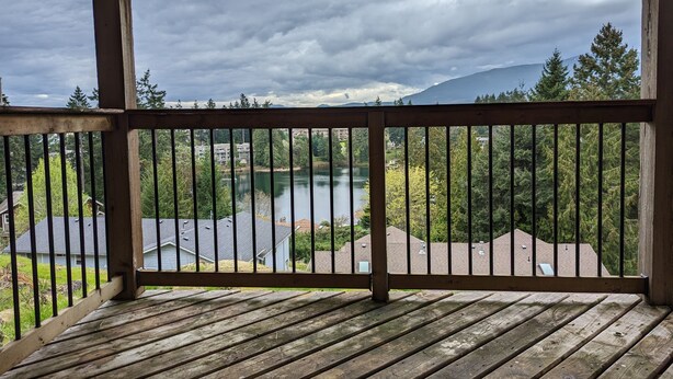 A wooden deck with a view of a lake, trees, and distant mountains.