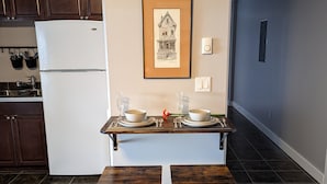 A kitchen with dark wooden cabinets, a white refrigerator, a framed artwork on the wall, and a small dining area with two stools.