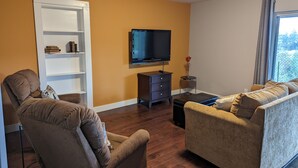 A living room with a sofa, armchair, TV, and a bookshelf.