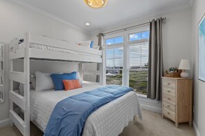 Una cama litera con colcha azul y blanca, un aparador de madera y una ventana con persianas.
