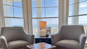 Une pièce avec deux fauteuils à motifs, une petite table avec une lampe et une vue sur l’océan.