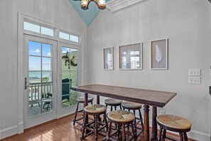 Un comedor con una gran mesa de madera y seis taburetes. Hay tres obras de arte enmarcadas en la pared.