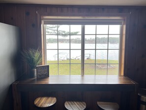 Interior de madera con un ventanal grande que da a un lago, una planta en maceta y un cuadro en el alféizar.