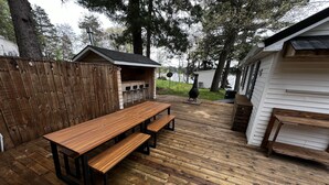 En træterrasse med et picnicbord, bænke, grill og en lille træbygning med skorsten.