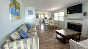 A spacious living room with a striped sofa, a wooden coffee table, and a fireplace. - The Reef Apartments Unit #2 - Downtown/5min walk to the beach! (Ocean City)