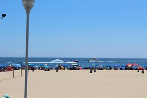 A beach with tents and umbrellas, a jet ski, and a boat in the water. - The Reef Apartments Unit #2 - Downtown/5min walk to the beach! (Ocean City)