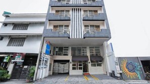 Ein mehrstöckiges Gebäude mit einem zentralen Eingang, Balkonen und einem Geschäft im Erdgeschoss.