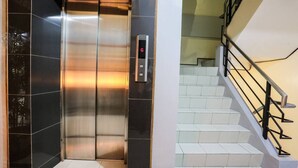 Ein Aufzug mit digitaler Anzeige neben einer Treppe mit Metallgeländer.