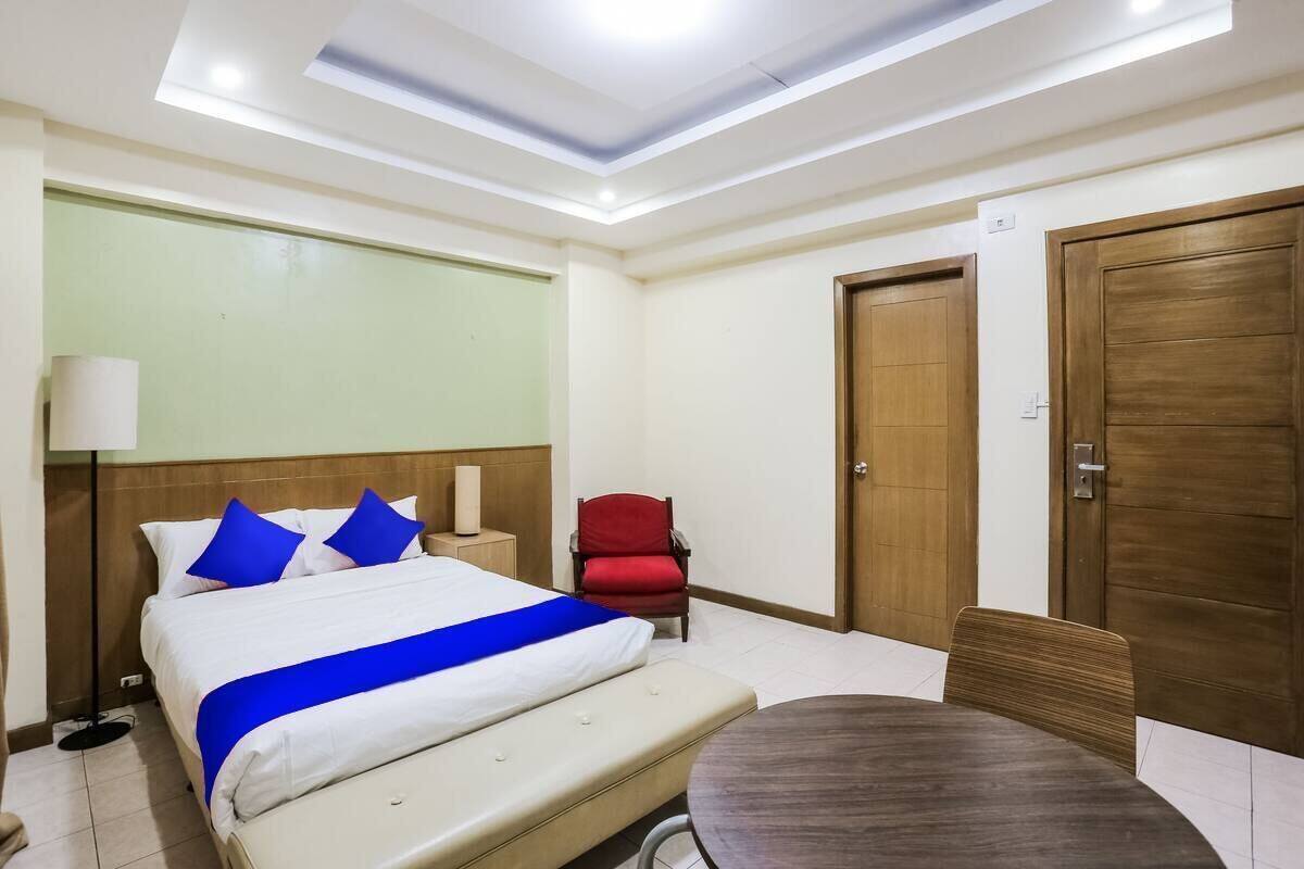 A hotel room with a bed, a red chair, a wooden door, and a round table.