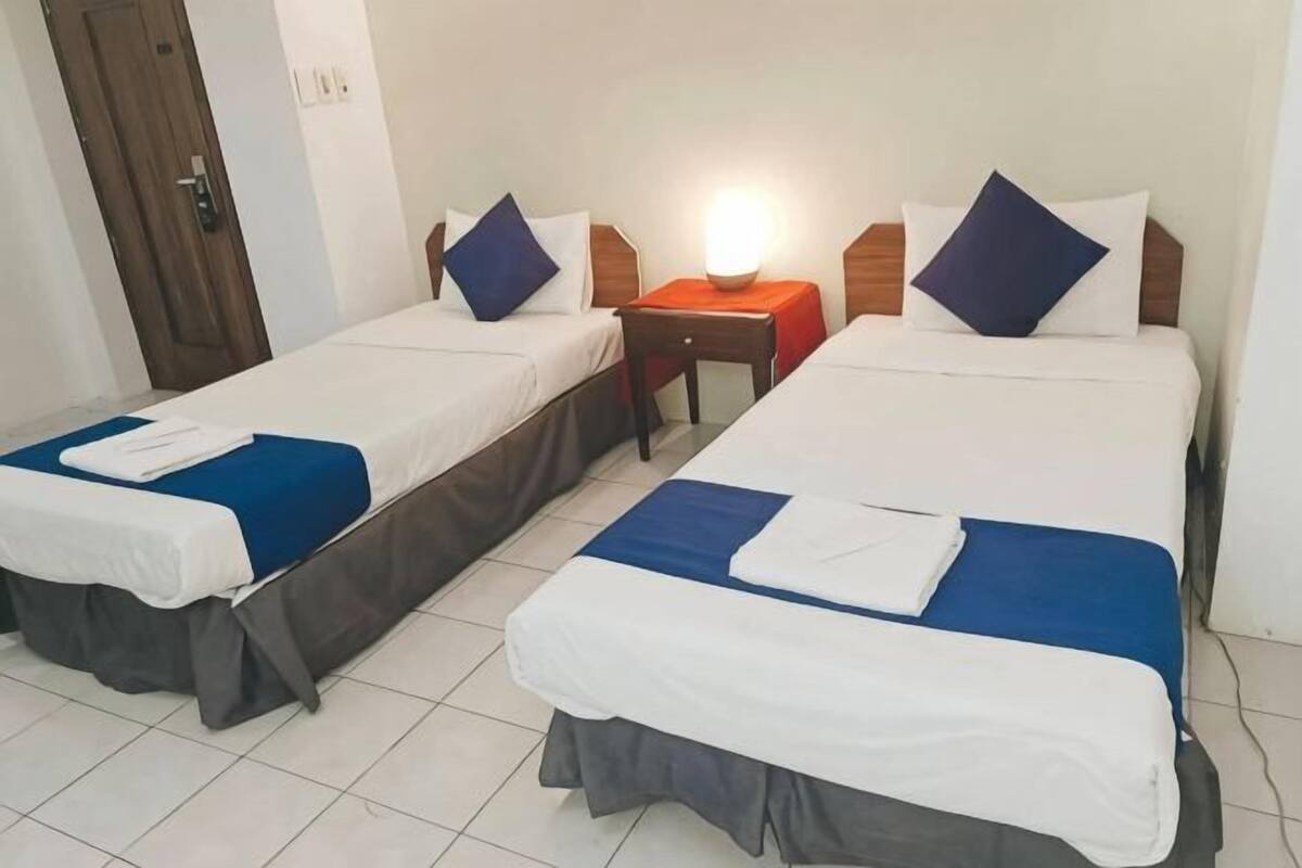A hotel room with two single beds, a nightstand, and a door.