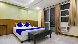 Ein Hotelzimmer mit Bett, einer Sitzbank, einem Fenster mit Vorhängen und einer Klimaanlage.