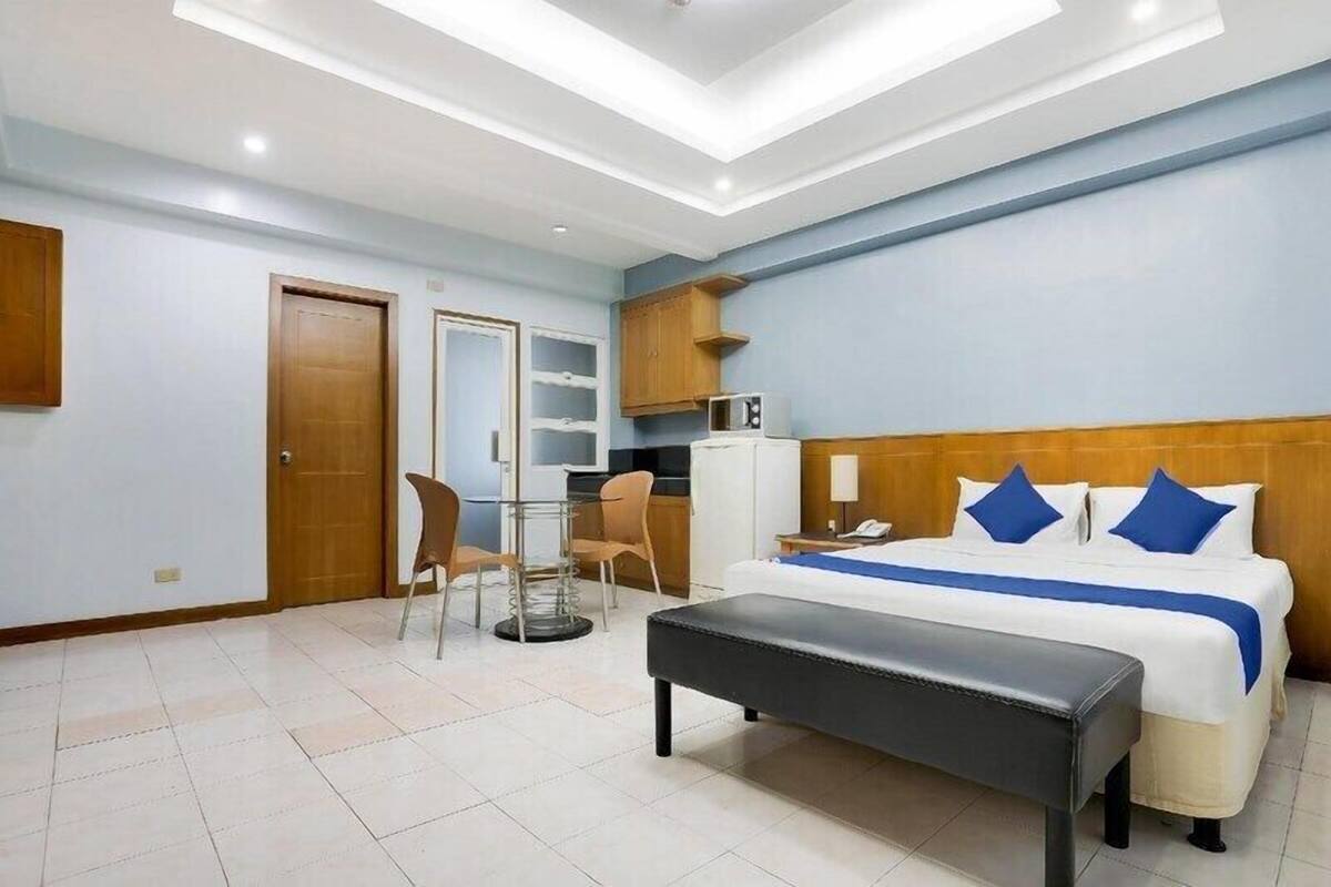 A hotel room with a bed, a desk, a chair, a bench, a microwave, and a wardrobe.