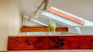 A modern interior with a sloped ceiling, skylight, wooden beams, and a hanging plant. - Quirky Downtown Loft (Harrisburg)