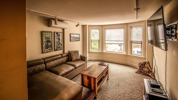 A living room with a brown leather sectional sofa, a wooden coffee table, and a flat-screen TV on a stand. - Quirky Downtown Loft (Harrisburg)