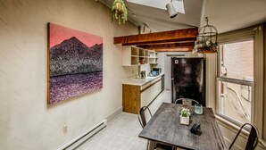 A modern kitchen with wooden beams, a dining table with chairs, and a large painting on the wall. - Quirky Downtown Loft (Harrisburg)