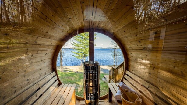 A circular wooden room with a view of a lake, a sauna, and a wooden bench.