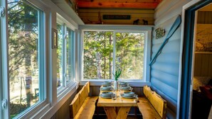 A cabin interior with a wooden bench table, a window with a view of trees, and a sign reading 'LAKE HOUSE'.