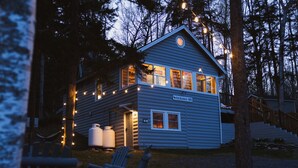 A two-story lodge with a porch, outdoor seating, and string lights.