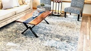 Un salon chaleureux avec un canapé, des fauteuils à motifs, un banc en bois et un tapis.