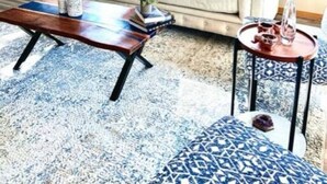Un salon avec un canapé beige, une table basse en bois et un tapis à motifs.