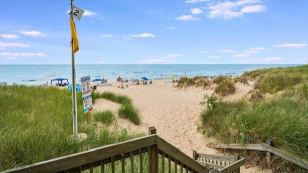 Une plage avec une promenade en bois menant au rivage, un drapeau et un panneau indicateur.