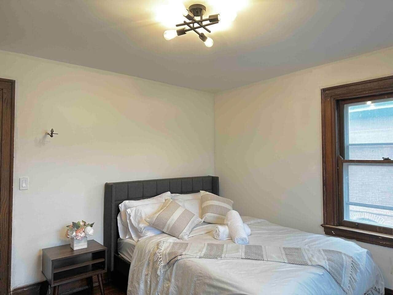 A bedroom with a bed, a nightstand, a window, and a ceiling light fixture.