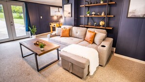 A modern living room with a sofa, ottoman, coffee table, and shelves with decorative items.