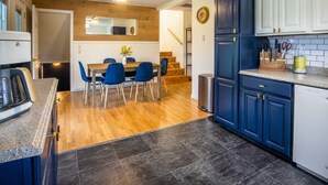 A compact kitchen with blue cabinets, a wooden dining table with blue chairs, and a small countertop with a coffee maker.