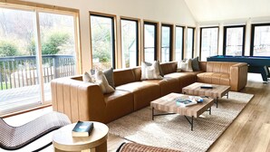 A spacious living room with a large sectional sofa, a pool table, and a view of the outdoors through large windows.