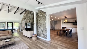 A spacious living room with a stone accent wall, a wooden dining area, and a staircase leading to an upper level.