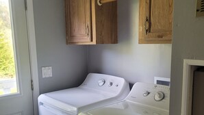 A compact laundry room with two stacked front-loading washers and dryers, wooden cabinets above, and a door with a doormat.