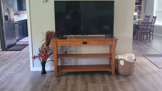 A living room with a wooden entertainment center, a flat-screen TV, a vase with flowers, and a woven basket.