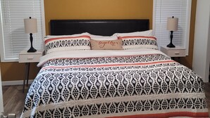 A bedroom with a bed, two bedside tables, a headboard, and a window with blinds.