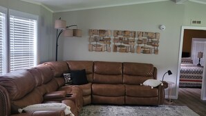 A living room with a brown leather sectional sofa, a patterned rug, and a wall art piece.