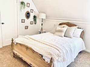 Een slaapkamer met een houten bed, witte beddengoed, een wandlamp en lijstjes met foto's.