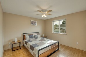 Une chambre à coucher avec un lit, un ventilateur de plafond, une fenêtre et un tableau au mur.